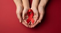 Hands holding red awareness ribbon on red background symbolizing support for HIV AIDS cancer heart disease and health advocacy campaigns.