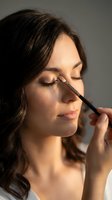 Young woman applying eyeshadow with makeup brush during beauty routine. Professional cosmetics application for daily skincare and glamour preparation.