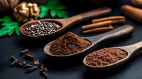 Dark aromatic spices and seasonings in wooden spoons on black background, including ground cocoa powder, cinnamon sticks, cloves and whole spices for baking.
