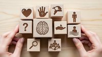 Hands arranging wooden blocks with mental health and wellness symbols including brain, heart, and mindfulness icons on light background.