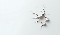 Cracked white surface with hole revealing light through broken plaster wall, dramatic destruction effect on plain background for creative design projects.
