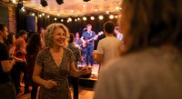 Joyful woman dancing at outdoor evening party with live band and string lights creating warm festive atmosphere for social gatherings and celebrations.