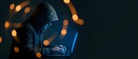 Hooded hacker typing on laptop in dark room with bokeh lights, cybercrime and data breach concept for security awareness.