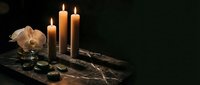 Spa wellness scene with burning candles, orchid flower and hot stones on dark slate surface creating relaxing atmosphere for massage therapy.