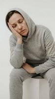 Tired woman in gray hoodie holding head and stomach showing exhaustion fatigue and discomfort on neutral background for health wellness concepts.