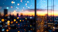 Blurred city lights and raindrops on window glass create dreamy bokeh effect against dramatic sunset sky, capturing urban atmosphere at dusk.