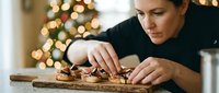Professional chef preparing gourmet appetizers on wooden board during Christmas season with festive tree lights creating warm holiday atmosphere.