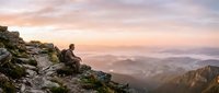Hiker sitting on rocky mountain peak at sunrise overlooking misty valley landscape, adventure and outdoor exploration concept for travel and nature themes.
