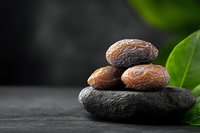 Fresh dates fruit stacked on dark stone with green leaves on blurred background for healthy eating and natural nutrition concepts.