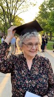 Happy senior woman celebrating graduation outdoors wearing cap and gown with family in background at university campus ceremony achievement milestone.