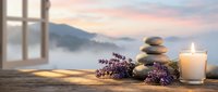Zen spa composition with balanced stones, lavender flowers and glowing candle on wooden surface overlooking serene mountain lake at peaceful sunset.
