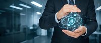 Business professional protecting digital security with hands around glowing shield icon in modern office environment for cybersecurity concepts.