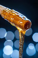 Golden honey dripping from wooden dipper with bokeh lights background for natural sweetness and organic food concepts.