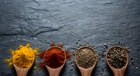 Colorful spices in wooden spoons on dark slate background. Turmeric, paprika, cumin and black pepper arranged in row for culinary cooking and seasoning concepts.