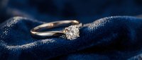 Elegant diamond solitaire engagement ring with round brilliant cut stone set in rose gold band resting on luxurious navy blue velvet fabric for jewelry display.