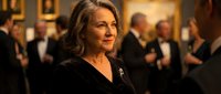Elegant mature woman in black evening dress at upscale social event with formal gathering in background for luxury lifestyle and sophisticated entertainment.