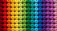 Colorful rainbow gradient of thread spools arranged in rows creating vibrant spectrum from red to purple for sewing and crafting projects.