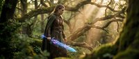 Young male elf warrior with glowing blue sword standing in mystical forest with golden sunlight filtering through ancient trees for fantasy gaming content.