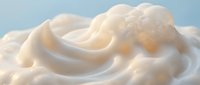 Creamy white whipped texture with soft swirls and foam bubbles, close-up macro shot on light blue background for food and beauty concepts.