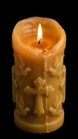 Ornate beeswax candle with carved cross and decorative elements burning with bright flame against black background for religious ceremonies and spiritual decor.