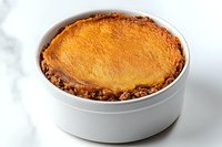 Mashed potato topping and seasoned minced meat filling in white ceramic ramekin on marble surface, traditional British comfort food.