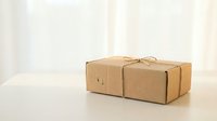 Brown cardboard packages tied with string on wooden surface against soft curtain background for shipping and delivery concepts.
