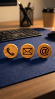 Wooden contact icons with phone, email, and at symbol on blue desk pad next to keyboard and coffee cup for business communication.