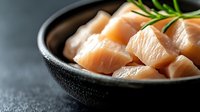 Fresh raw salmon cubes in black ceramic bowl with rosemary sprig on dark stone background, selective focus. Healthy seafood cooking ingredients.