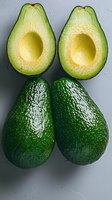 Fresh ripe avocados, whole and halved showing creamy yellow flesh and pit cavity on light background. Clean minimal food photography for healthy eating.