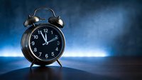 Black vintage alarm clock showing nearly midnight on dark blue background with dramatic lighting for time management concepts.