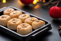 Fresh baked cinnamon rolls with nuts on black baking tray against dark background with festive Christmas decorations and bokeh lights.