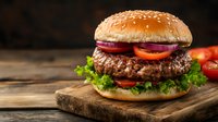 Fresh juicy beef burger with lettuce, tomato and red onion rings on rustic wooden cutting board against dark background. Classic American fast food.