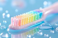 Colorful rainbow toothbrush with multicolored bristles on bright blue background with water droplets and bokeh lights for dental hygiene and oral care.