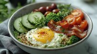 Breakfast bowl with fried egg, bacon, cucumber, tomato, broccoli and quinoa grain base. Healthy morning meal for nutrition and wellness content.