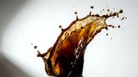 Dynamic coffee splash with droplets frozen in motion against neutral background for beverage advertising and commercial use.