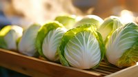 Fresh green cabbage heads cut in half showing crisp white interior texture and layered leaves on wooden surface in natural lighting.