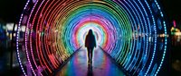Person walking through illuminated rainbow tunnel with colorful LED lights creating circular patterns for futuristic technology and digital art concepts.