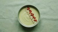 Green smoothie bowl topped with goji berries and hemp seeds in a ceramic bowl, flat lay on sage linen background, healthy breakfast.
