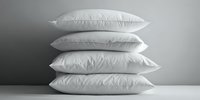 Stack of four white fluffy pillows arranged vertically against gray wall on white surface for bedroom decor and comfort sleep concept.