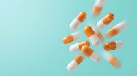 Orange and white capsules scattered on turquoise background with motion blur effect for pharmaceutical and healthcare design concepts.