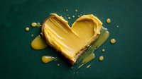 Golden heart-shaped butter melting with droplets on dark green background for cooking and baking concepts.