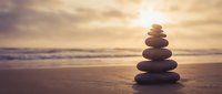 Balanced stone stack on sandy beach at golden sunset creating peaceful zen meditation atmosphere for wellness and mindfulness practices.