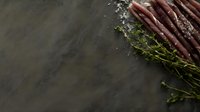 Fresh purple carrots and aromatic thyme sprigs scattered with sea salt crystals on dark stone background, corner composition with copy space for food styling.