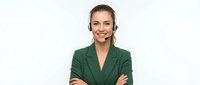 Professional young Caucasian businesswoman with headset smiling confidently with crossed arms in green blazer for customer service and telemarketing.