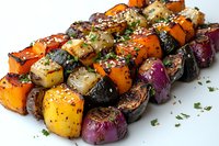 Grilled vegetable skewers with colorful bell peppers, red onions, and butternut squash chunks, seasoned with herbs and sesame seeds on white background.