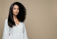Young mixed-race woman with curly and straight hair styling in white casual top against neutral beige background for beauty and fashion concepts.
