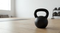 Black kettlebell weight on wooden floor in bright gym studio with window light, ready for strength training and fitness workouts.