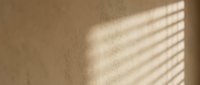 Sunlight streaming through window blinds creates soft parallel shadows on a neutral beige wall, ideal for backgrounds and design overlays.