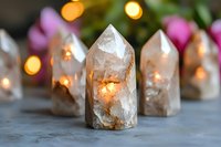 Crystal quartz points with glowing warm light inside on gray concrete surface, bokeh lights and pink flowers in background, spiritual healing atmosphere.