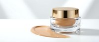 Luxury cosmetic jar with golden cap and foundation cream smear on white background. Premium skincare product for beauty and makeup routine.
